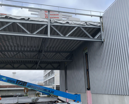 Auskragende Stahlkonstruktion des Hallenvordachs während der Montage am Werk von Wagner Fahrzeugteile mit dem Hubsteiger